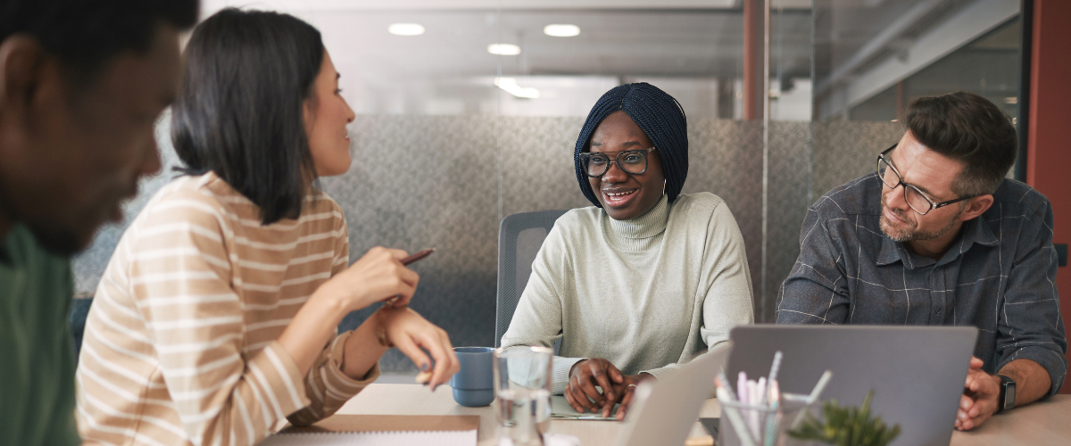 A team of people are sat at a boardroom table conversing.
