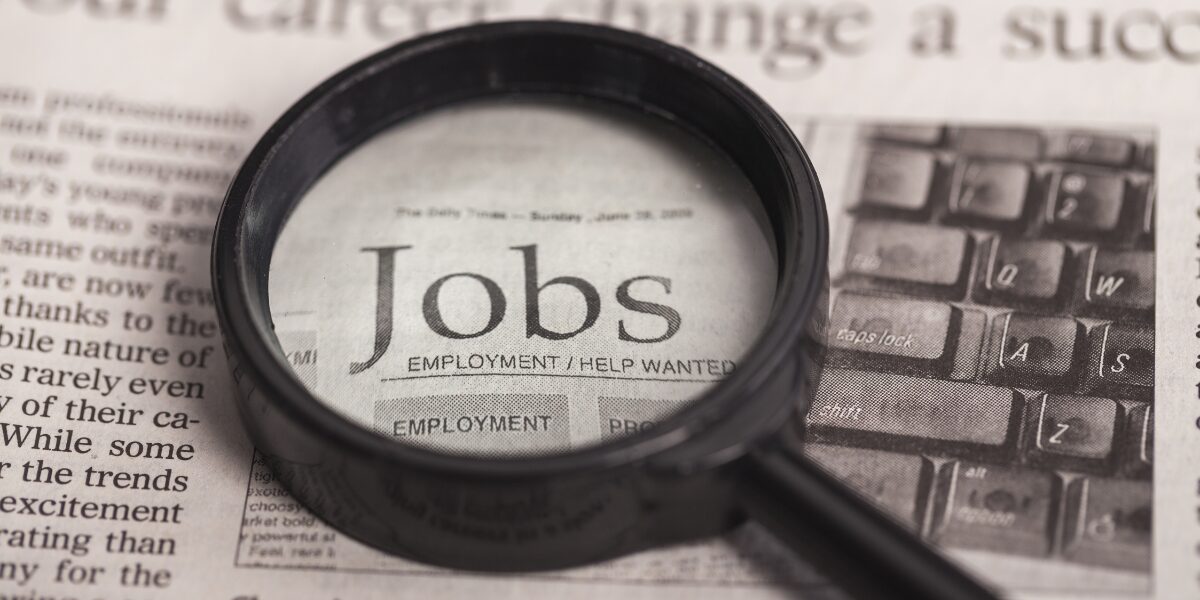 A magnifying glass is laying on top of a newspaper with the word "Jobs" magnified.