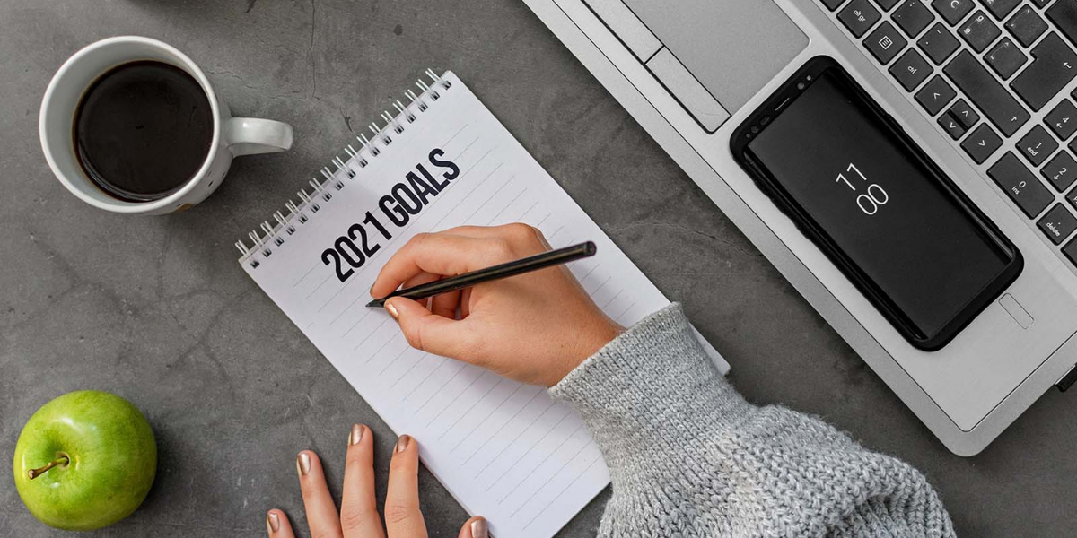 A woman sitting at a desk writing on a 2021 notepad.