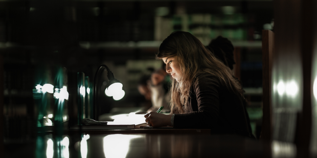A woman working in a dark room writing in a notebook on a table.