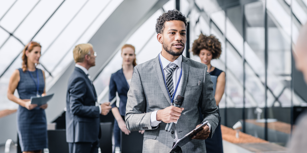 A man holding a microphone standing in an office building with colleagues.