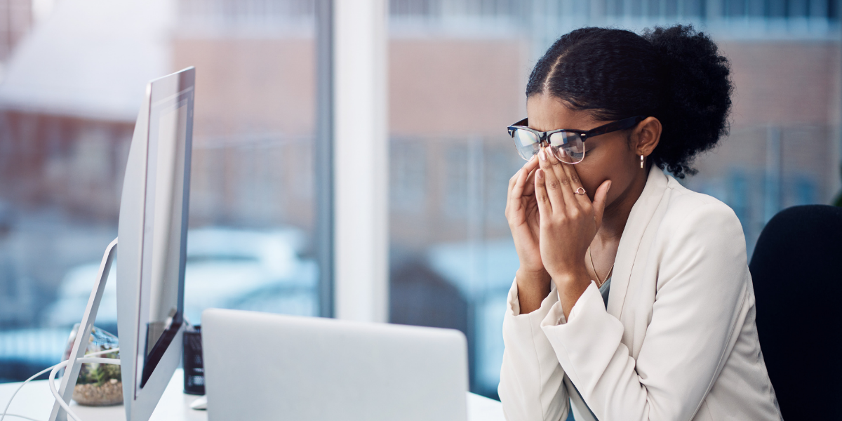 A woman is sat at her laptop with her hands covering her face.