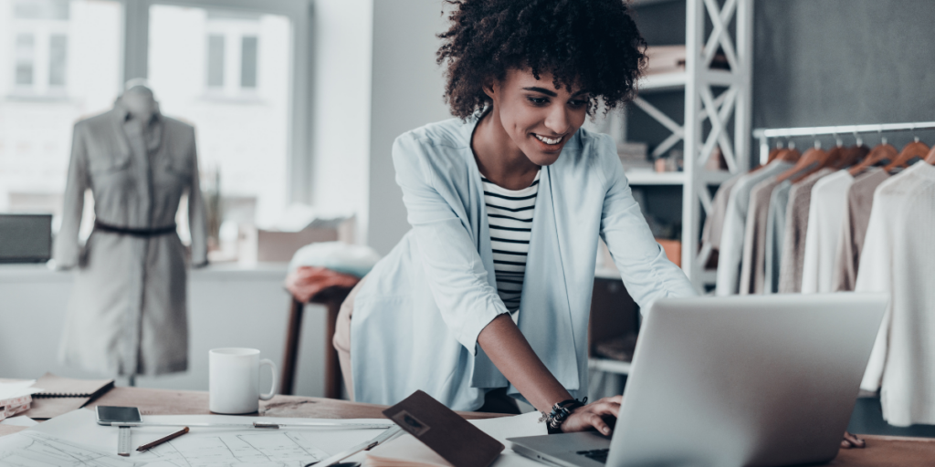 A woman is standing at her desk typing on her laptop.