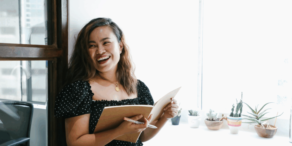 A woman is stood reviewing paperwork and smiling at the camera.