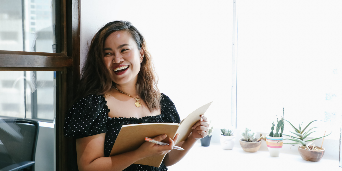 A woman is stood reviewing paperwork and smiling at the camera.