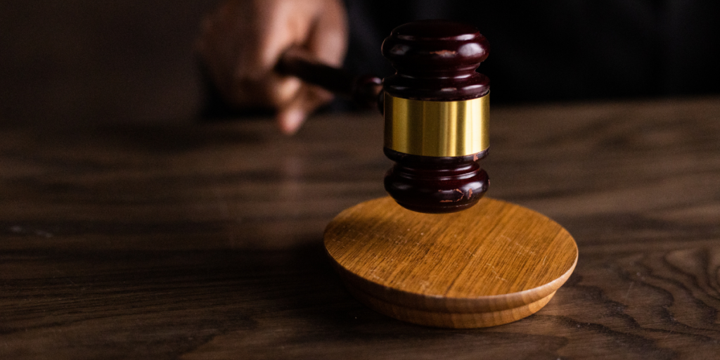 A hand holding a wooden gavel on a wooden table.