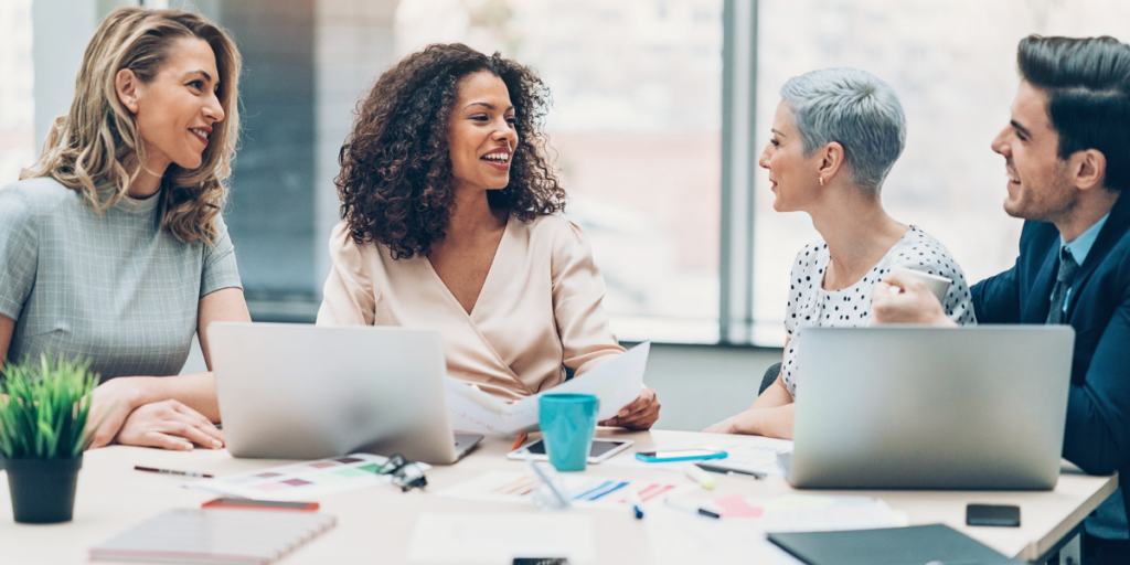 A group of four people are sitting at a boardroom table conversing.
