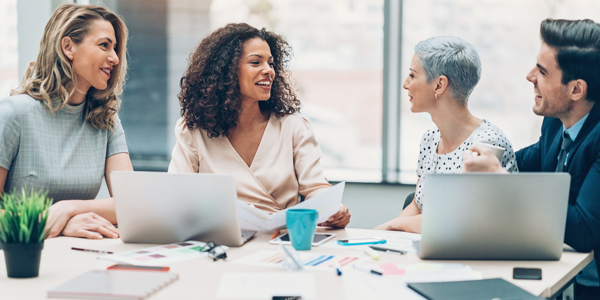 A group of four people are sitting at a boardroom table conversing.