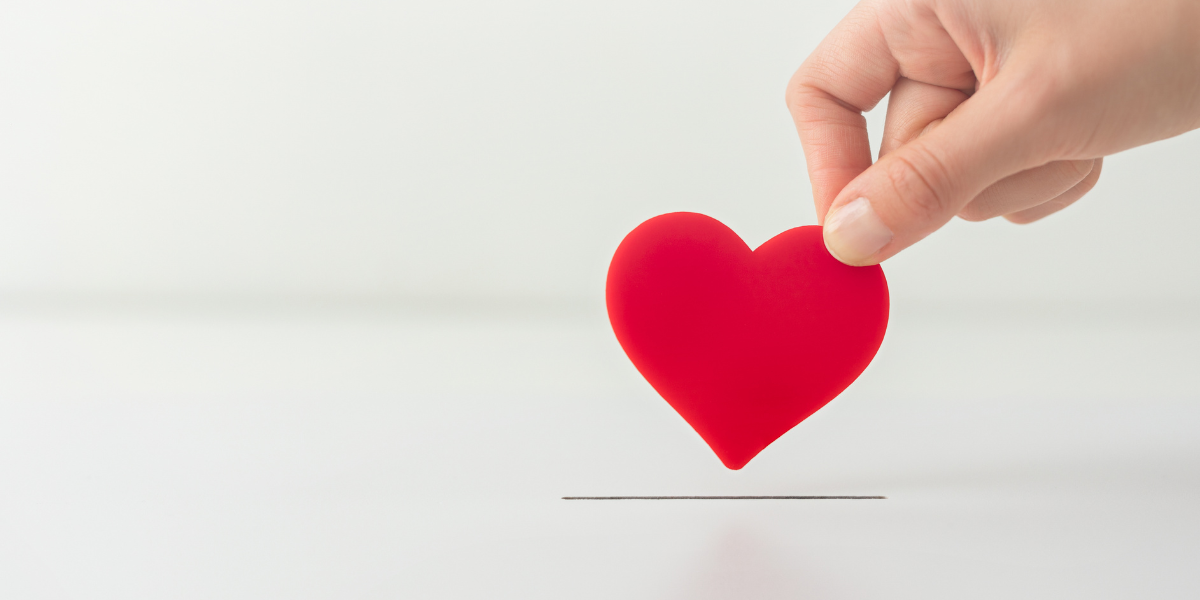 A hand is holding a red foam heart above a slot in a white box.