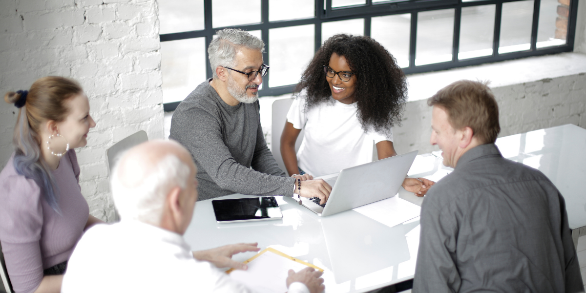 A group of people are sat at a boardroom table conversing and collaborating.