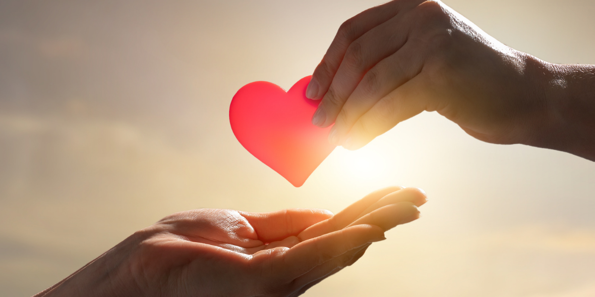 One hand is handing another a red plastic heart.