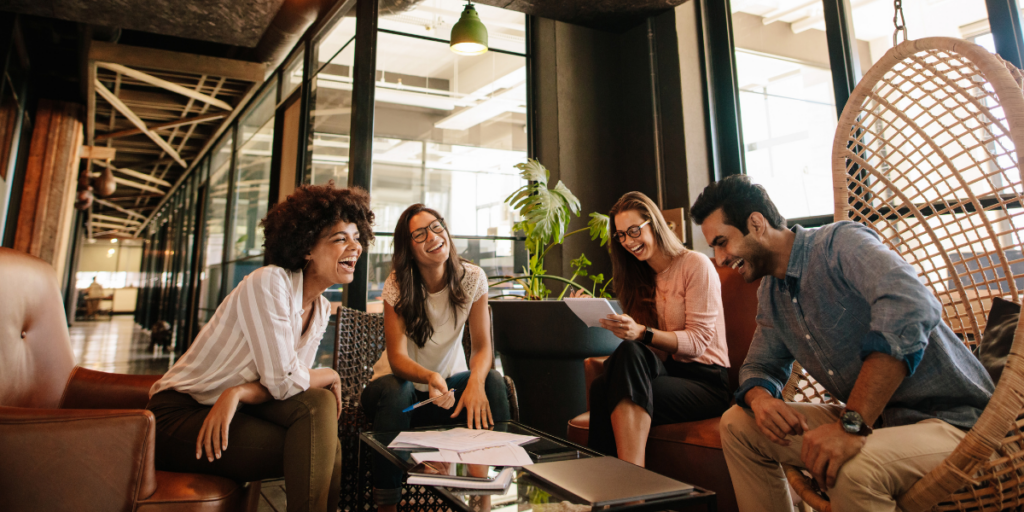 A team of four people sitting in an open office space conversing.
