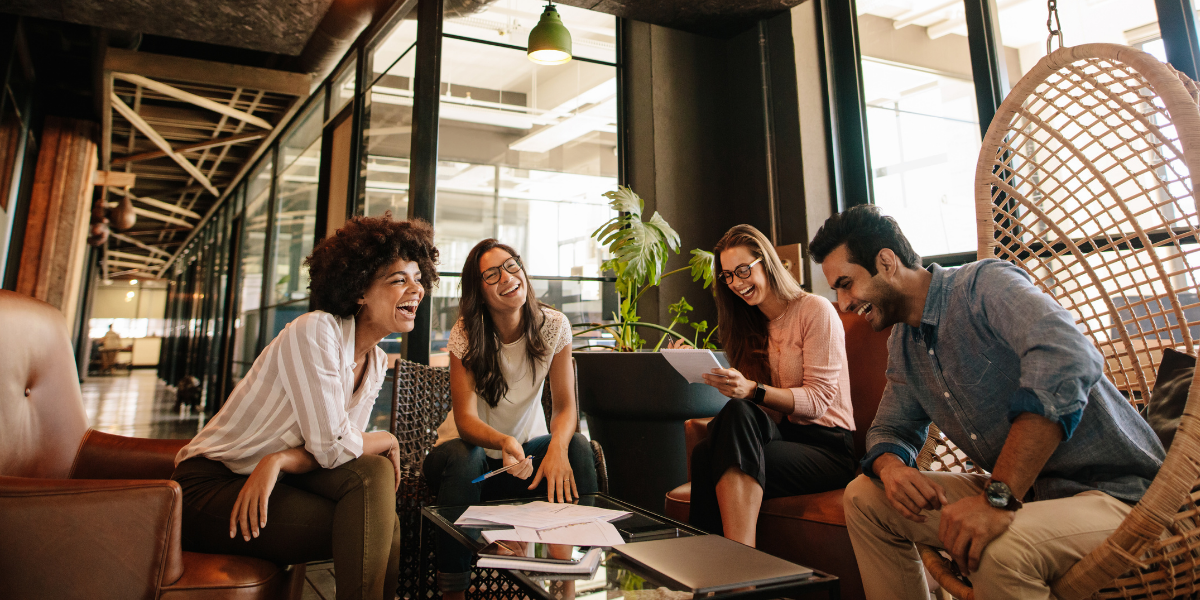 A team of four people sitting in an open office space conversing.