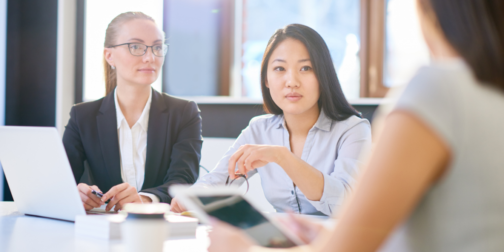 Three people are sitting at a boardroom table conversing.