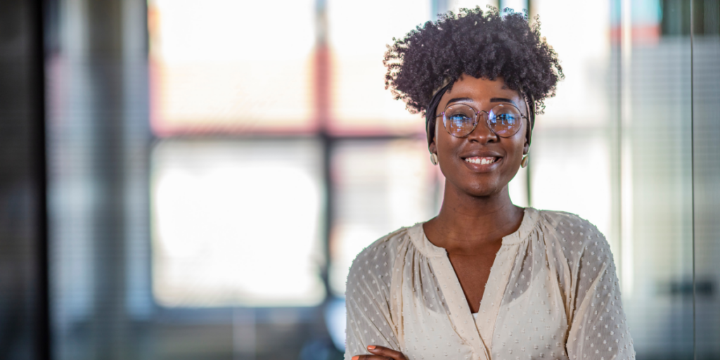 A woman is standing in an office smiling at the camera.