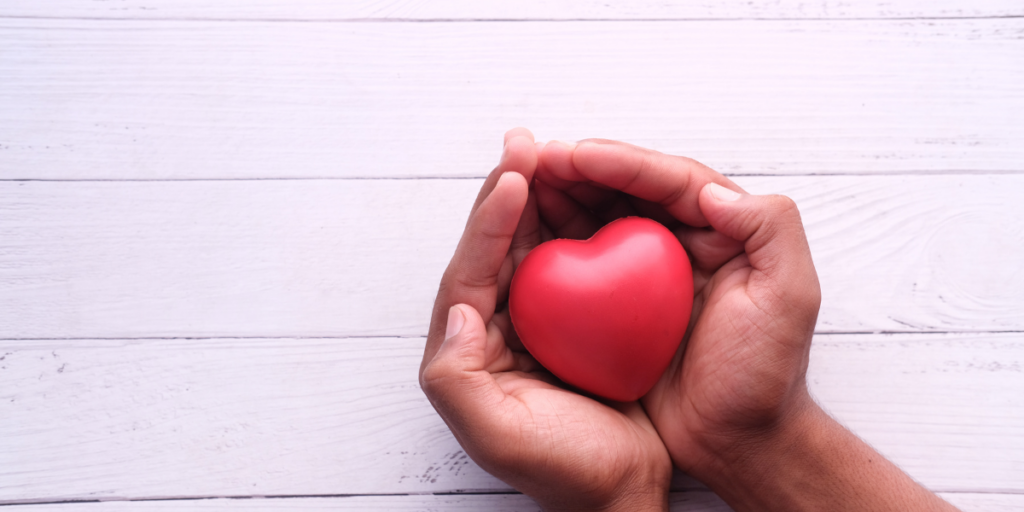 Two hands holding a red foam heart are resting on a white table.