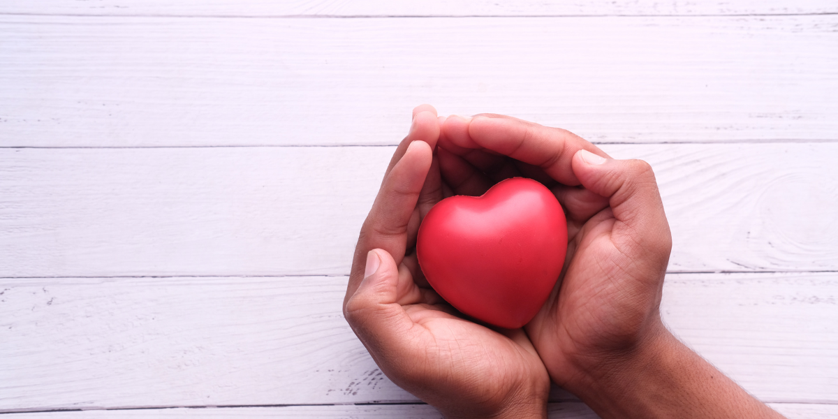 Two hands holding a red foam heart are resting on a white table.