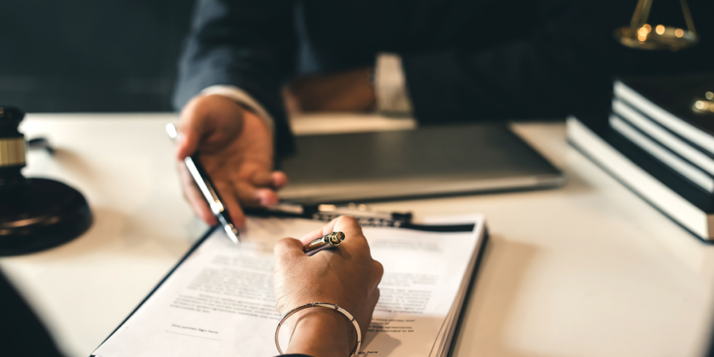 Two people sitting at a table and one person is signing a contract.