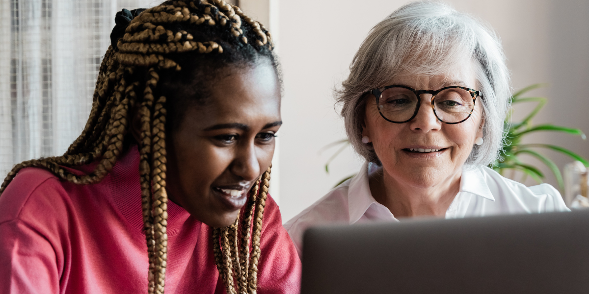 Two women are sat at a desk reviewing a laptop screen.