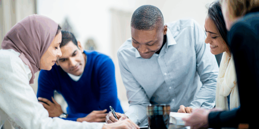 A team of people are surrounding a boardroom table reviewing a document.