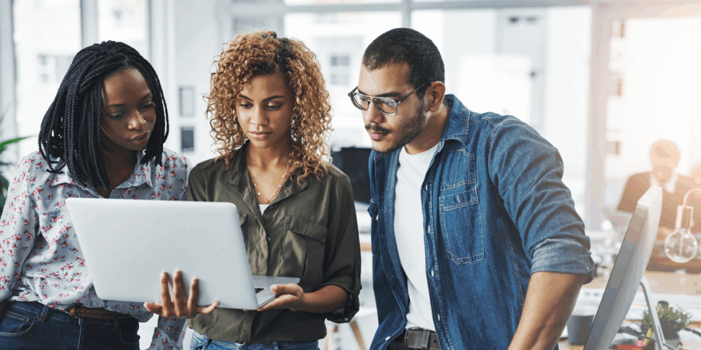 Three people standing next to one another - the woman in the centre is holding the laptop.