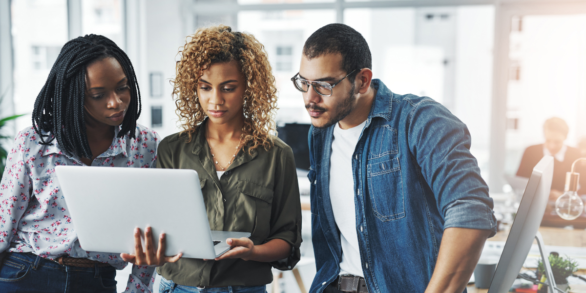 Three people standing next to one another - the woman in the centre is holding the laptop.