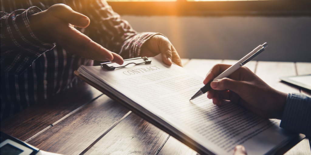 Two people sitting at a table and one person is signing a contract.