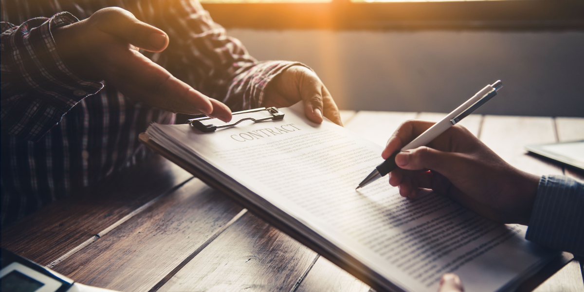 Two people sitting at a table and one person is signing a contract.