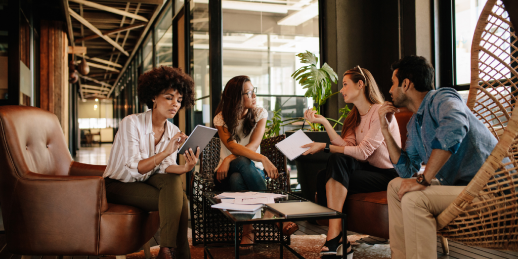 A team of four people sitting in an open office space conversing.