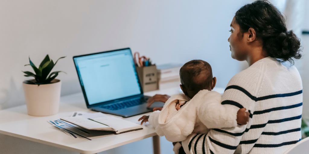 A woman sat at her desk working and holding her baby.