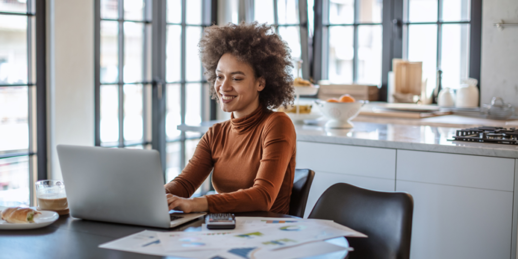 A woman sitting at dining room table working on laptop.