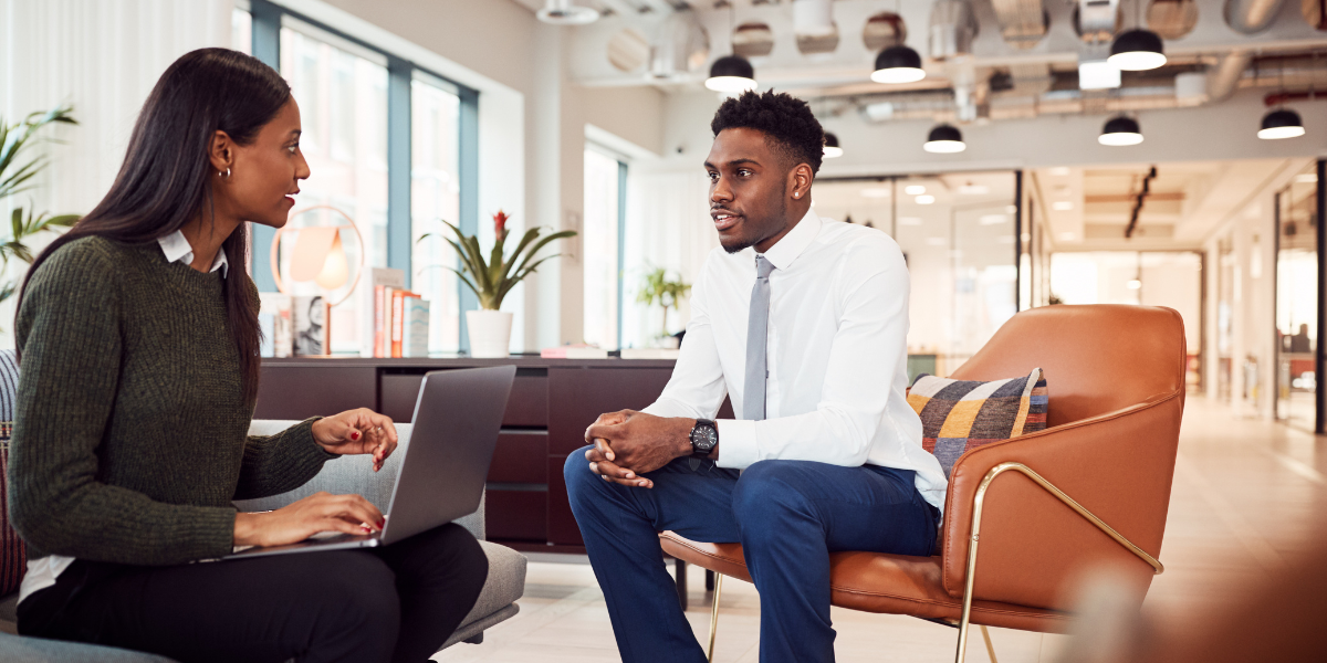 Two people are sat across from each other in an office conversing.