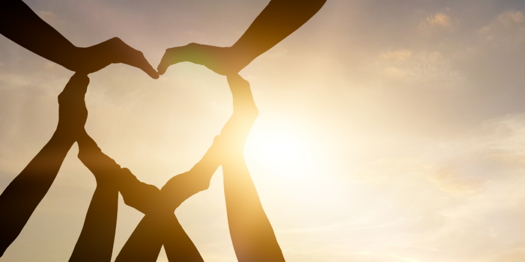 Hands raised in the air making a heart shape outside in the sun.