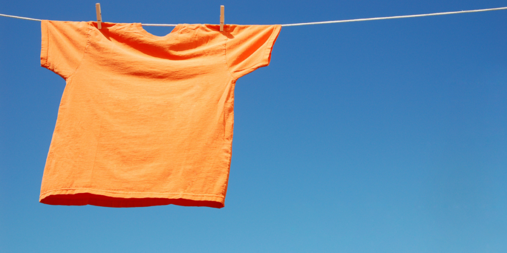 Orange shirt hanging on clothes line. Clear blue skies behind.