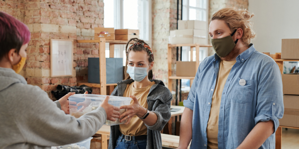 Three volunteers wearing medical-grade masks are volunteering at a clothing drive.