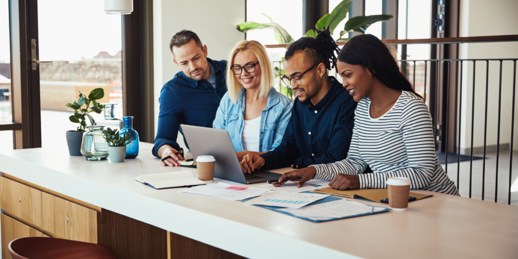A group of people are convened at a desk collaborating on a project and conversing.
