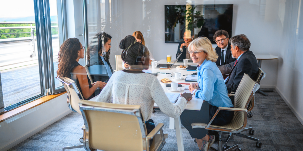 A team of people are sat in a boardroom conversing amongst each other.