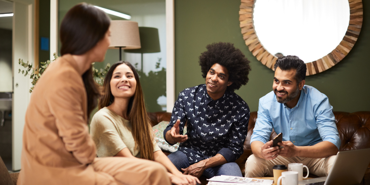 A group of people are sat in a circle conversing and laughing.