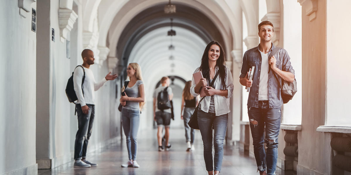 Two people are walking down a corridor of a university holding books and school bags.