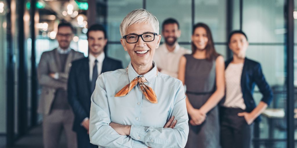 A woman stands in front of a group of colleagues smiling at the camera.