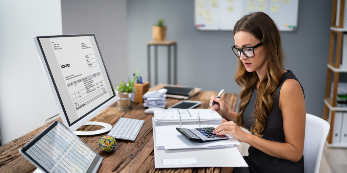 A woman is sitting at a desk writing notes and reviewing financial documents.