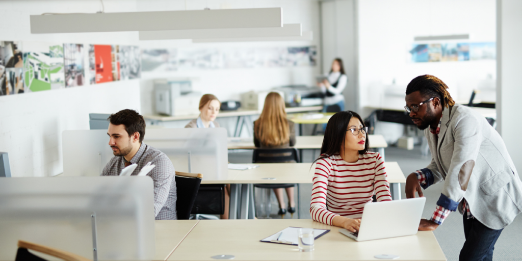 A group of people in an office space working. A woman and man are conversing.