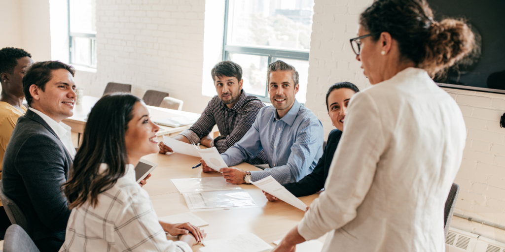 A team meeting in a boardroom. A woman is stood presenting to the team.