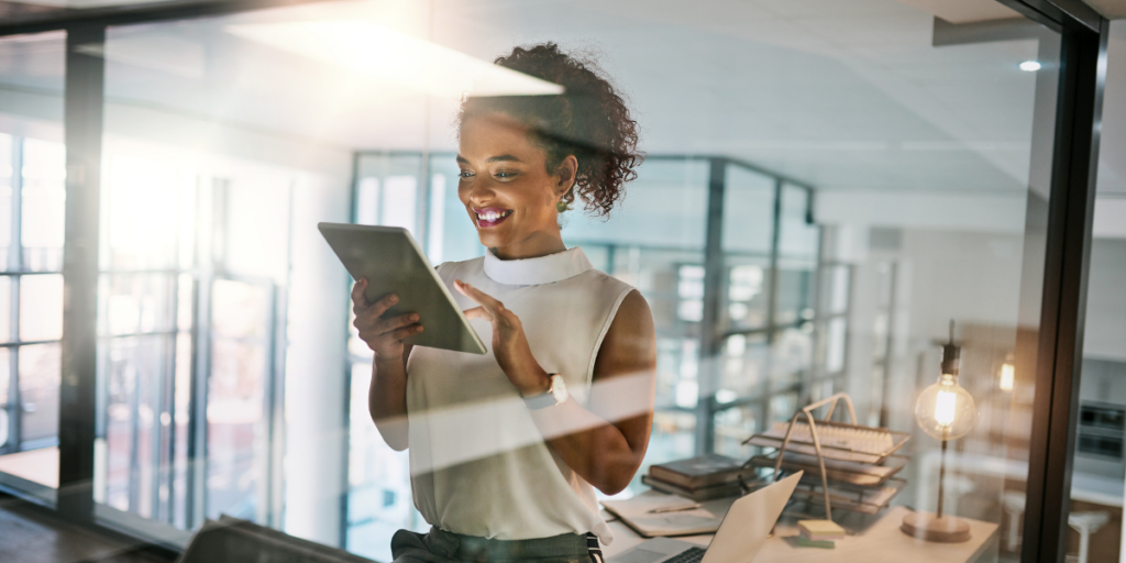 A woman is stood in an office holding a tablet.