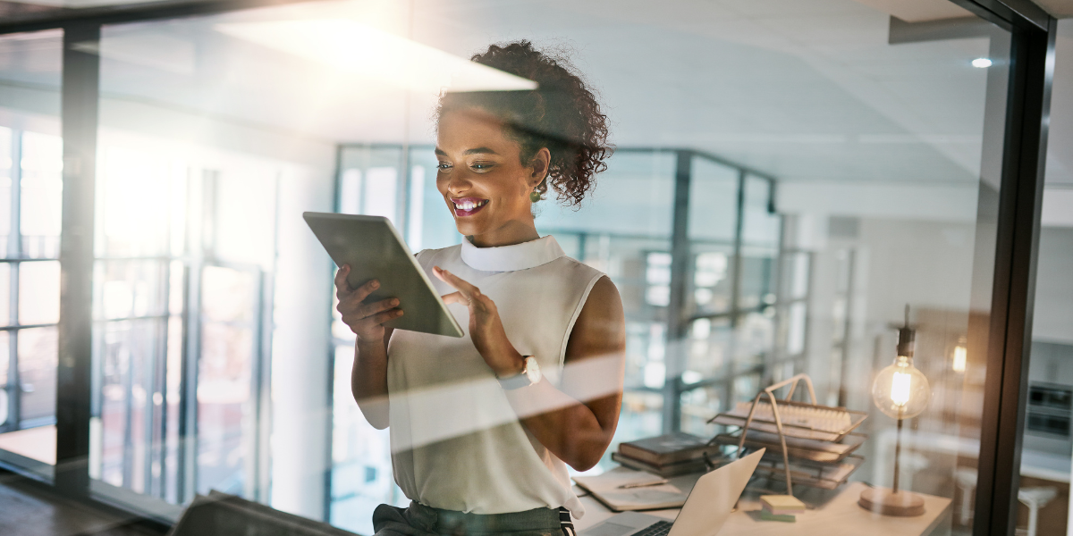 A woman is stood in an office holding a tablet.