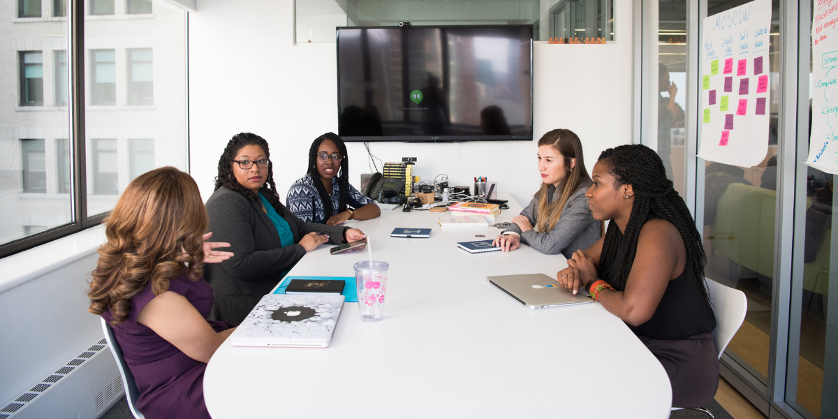 A group of women are sat in a boardroom conversing.