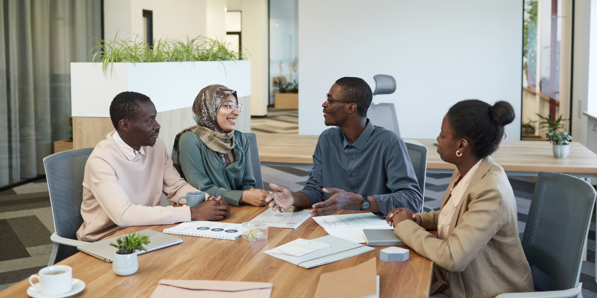 Four people are sat at a boardroom table conversing.