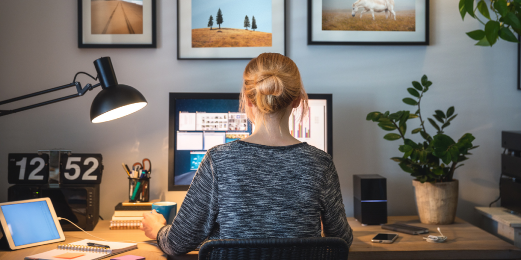 A woman is sat at her computer working on a project in a dimly lit room.