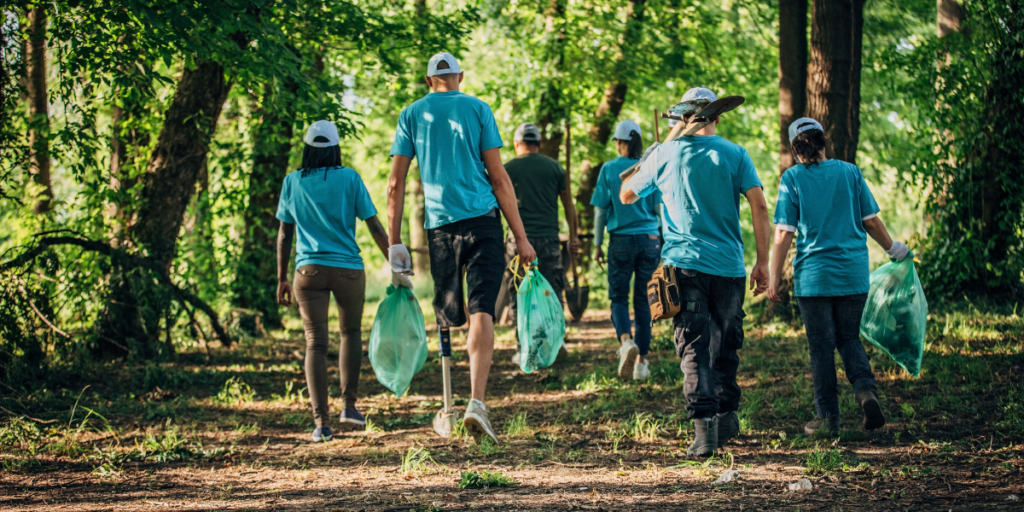 A group of volunteers wearing matching blue shirts volunteering in the forest cleaning up garbage.