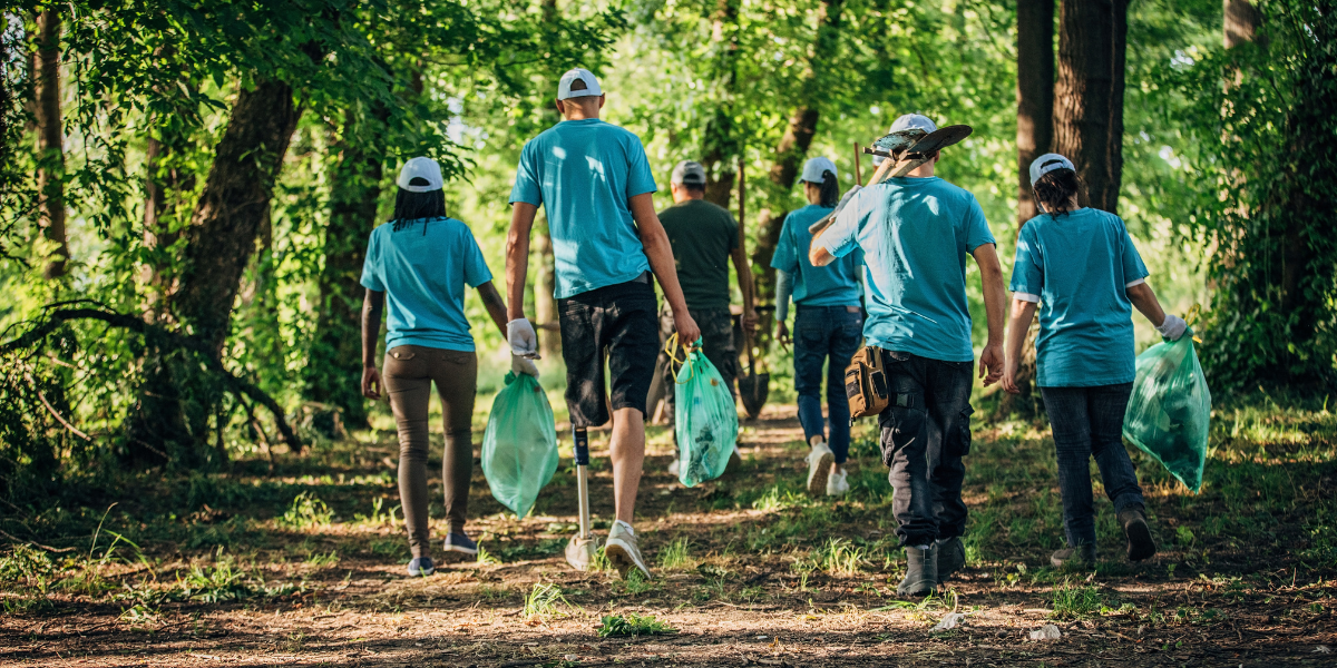 A group of volunteers wearing matching blue shirts volunteering in the forest cleaning up garbage.